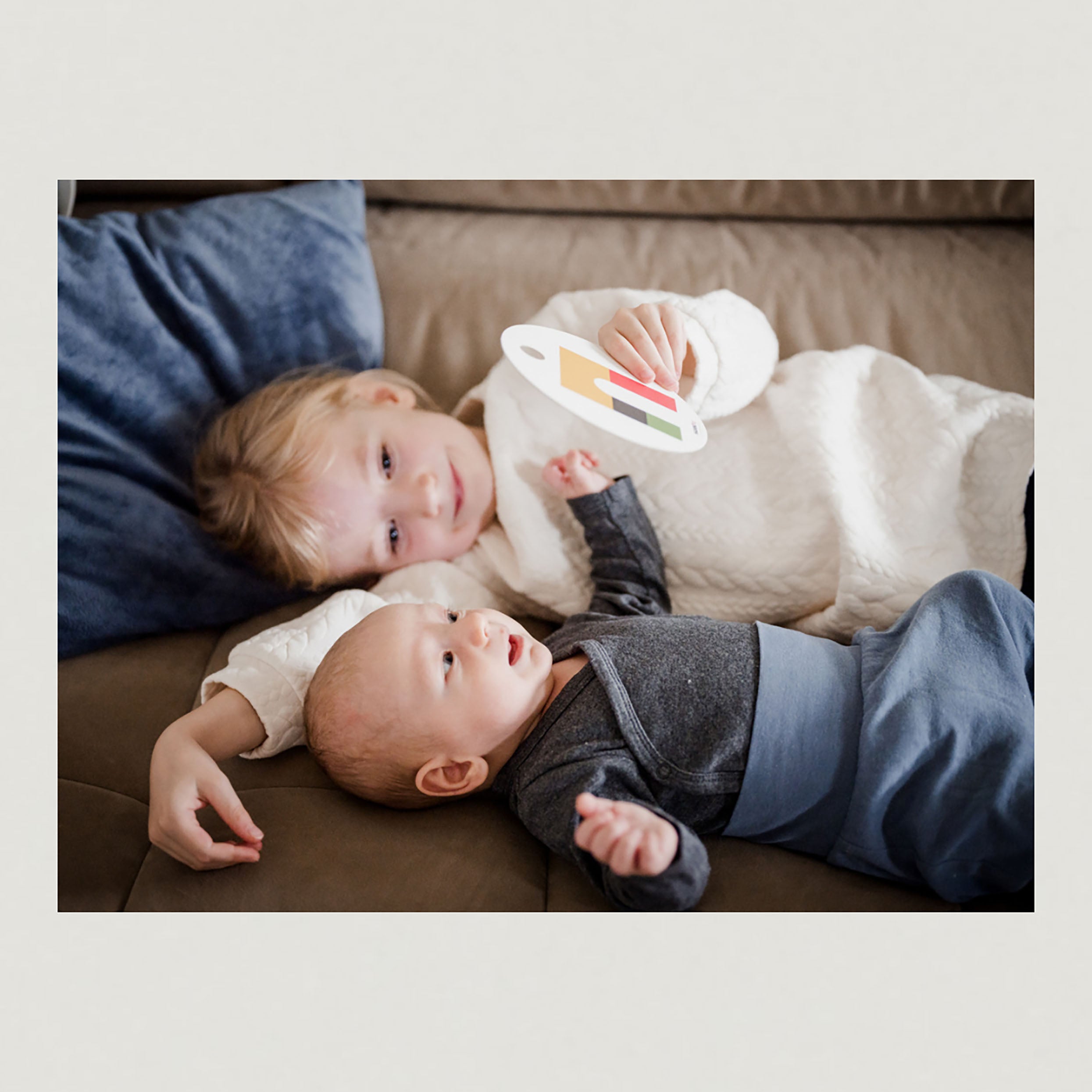 Foto Mädchen und Baby liegen auf der Couch mit Kontrastkarte in der Hand