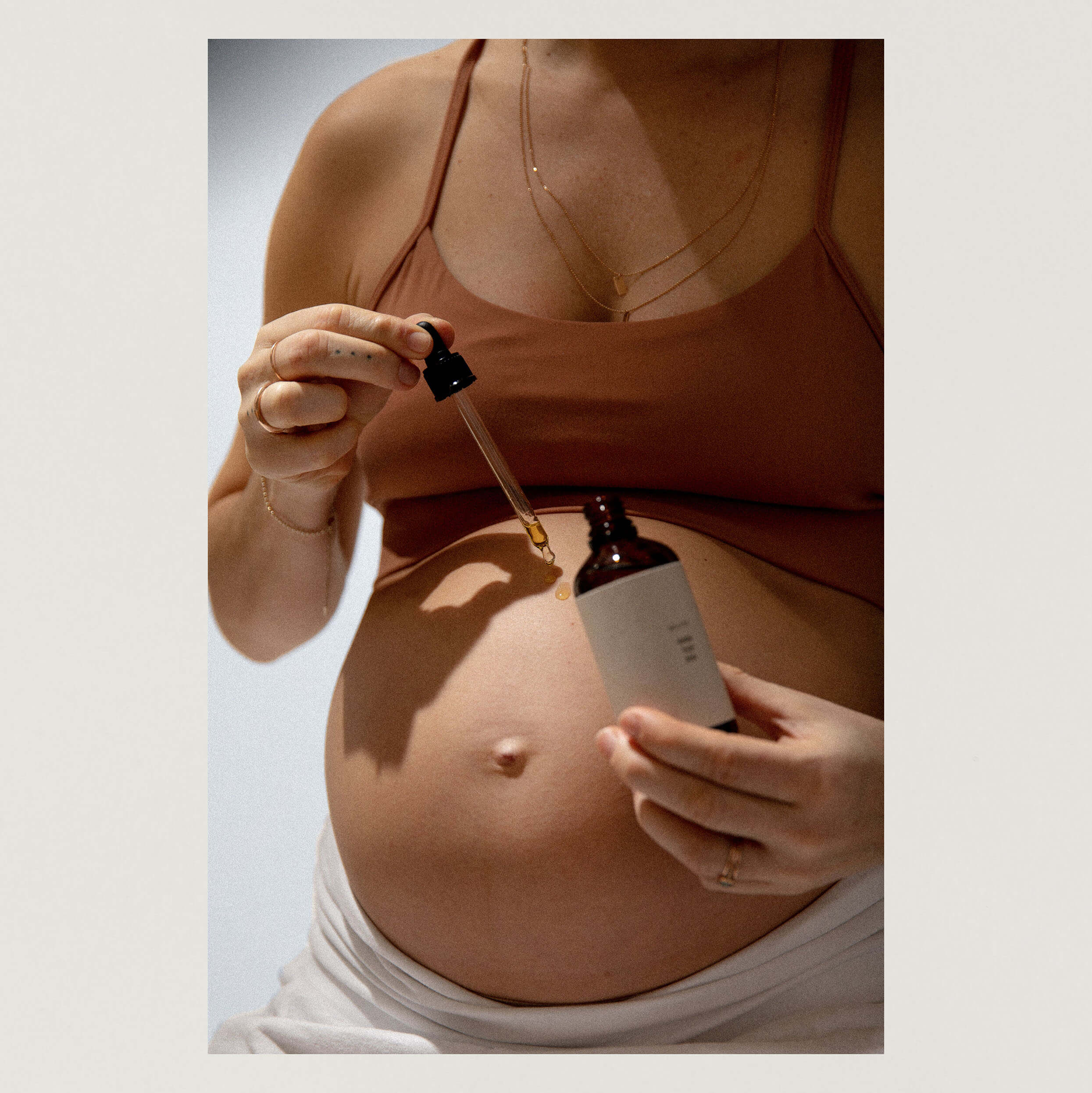 Foto des Bauchs einer Schwangeren, die mit einer Pipette Öl auf den Bauch tropft.