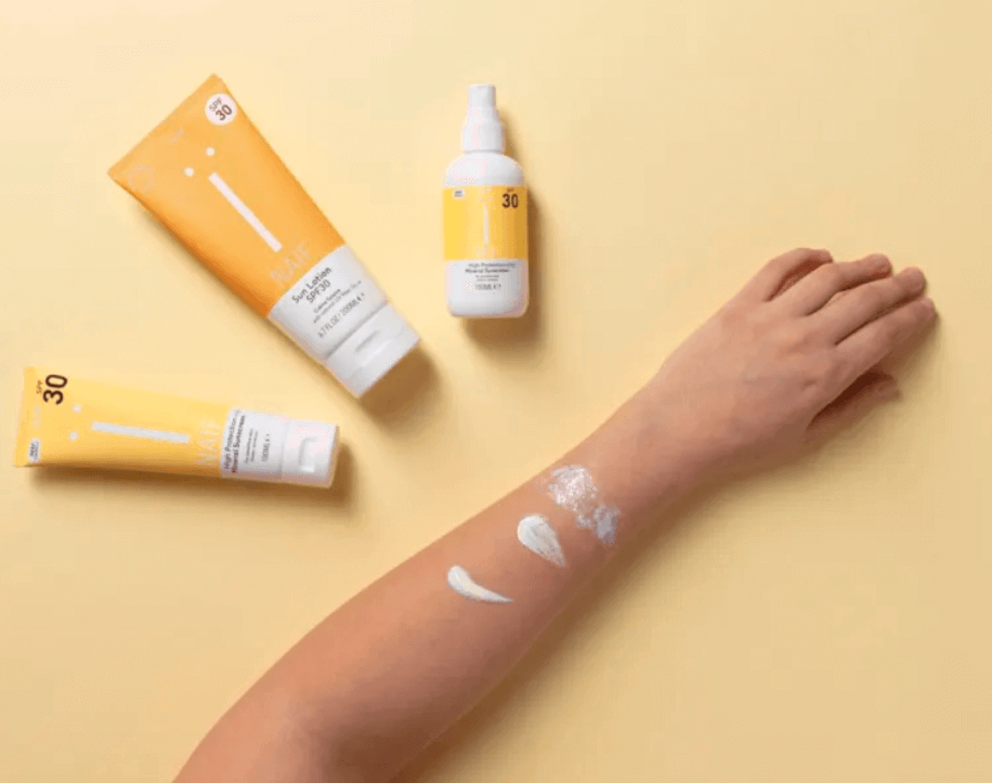 Foto mit Kinderarm, der mit Sonnencreme eingerieben wird und jeweils drei unterschiedliche Sonnencremes von Naif