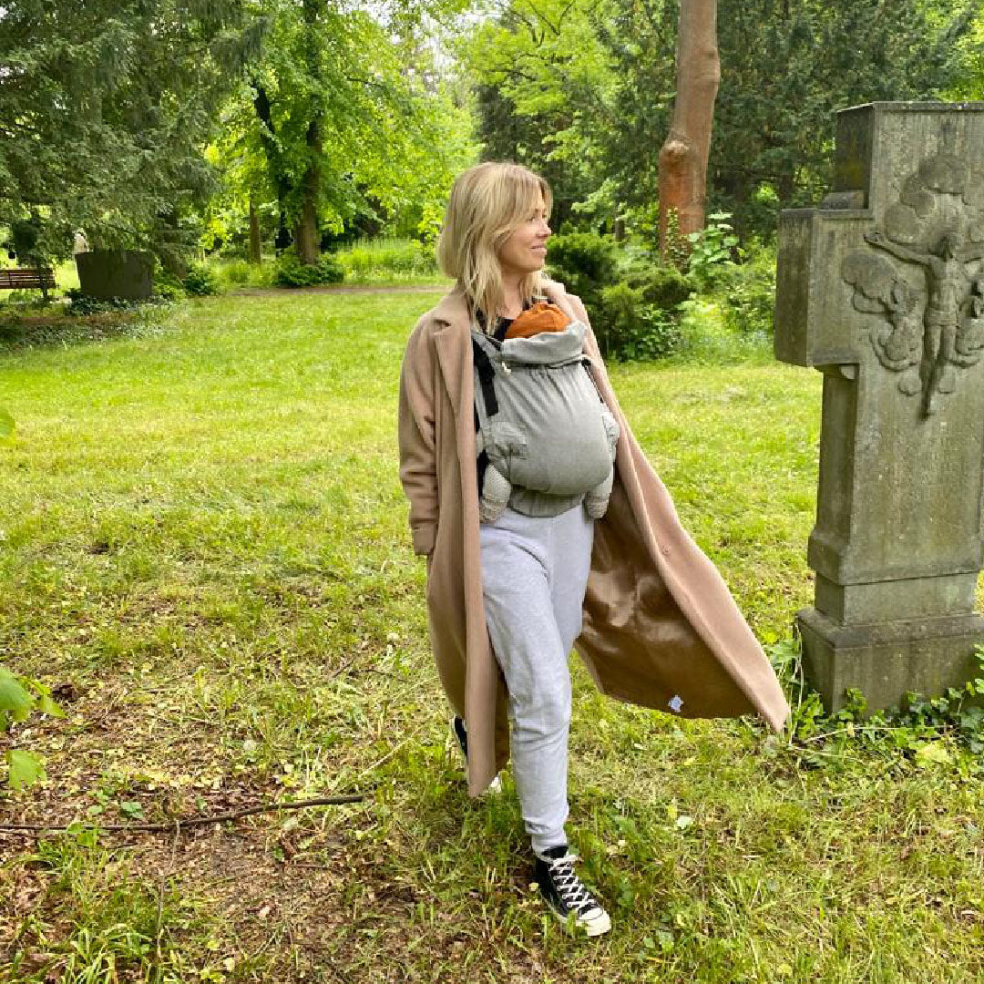 Foto einer Frau die ihr Kind in einer Trage auf dem Bauch trägt
