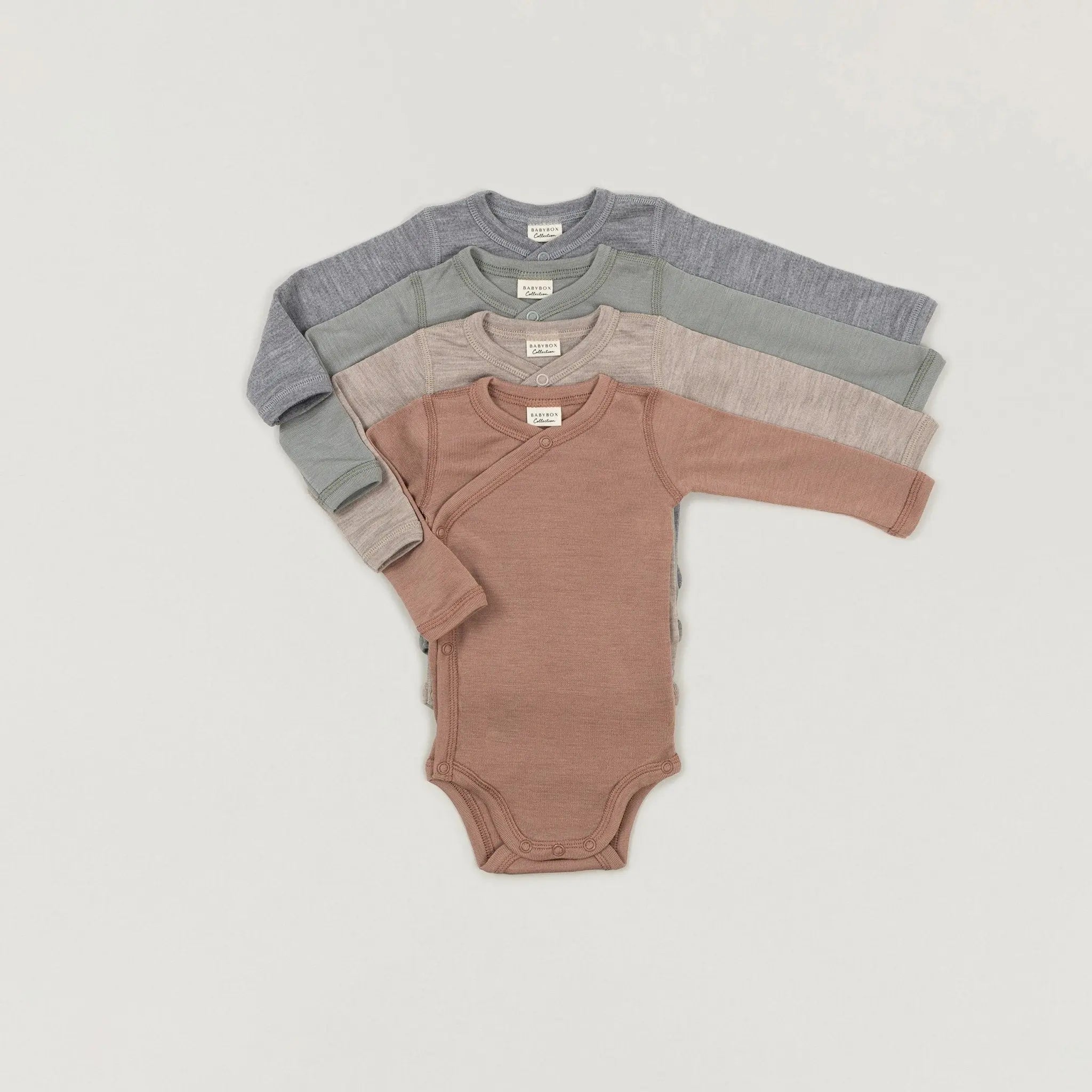 Ein Produktbild der verschiedenfarbigen Langarmwickelbodys aus Wolle und Seide der Babybox Collection übereinandergelegt in der Vorderansicht im Onlineshop von Babybox and Family #HIDDEN